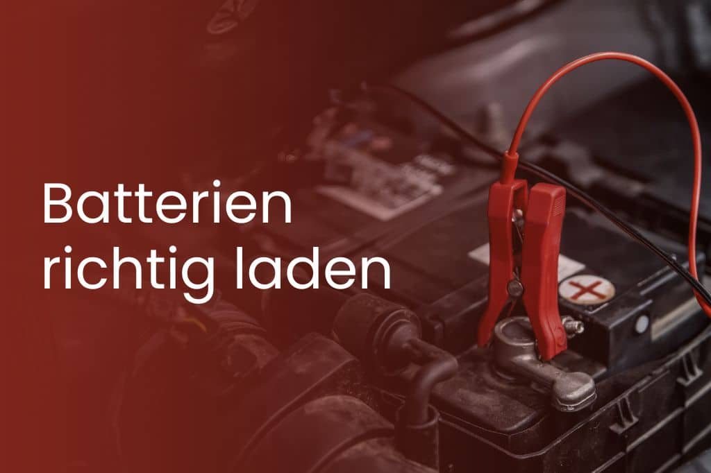 Nahaufnahme einer Autobatterie mit angeschlossenen roten Ladezangen, daneben der Schriftzug "Batterien richtig laden" auf rotem Hintergrund.