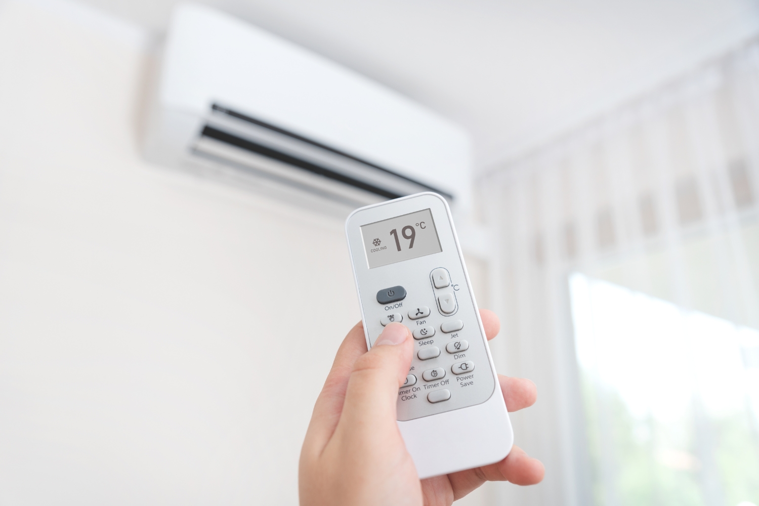 Hand with remote control sets an air conditioning system in the room to 19 °C cooling mode.