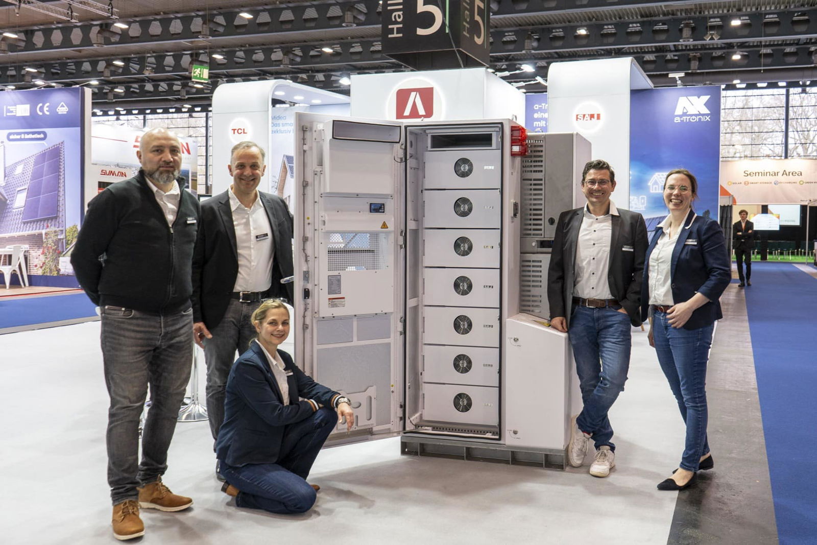 Team photo at the trade fair in front of an open SAJ CHS2 commercial storage unit. Five people pose smiling next to the storage unit on display, with the AKKU SYS stand in the background.