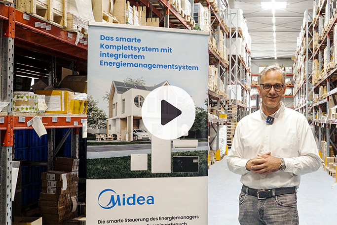 Midea-Komplettsystem mit Energiemanager im Lager präsentiert; Person steht neben Banner mit Haus- und Systemabbildung. Playbutton in der Mitte des Bildes.